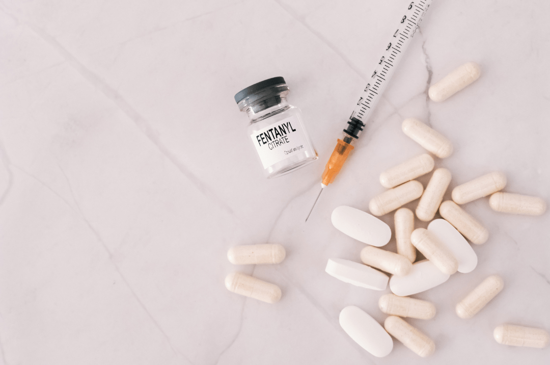 A bottle containing fentanyl, a syringe needle, and various pills, representing opioid medication and potential health risks of fentanyl overdose.