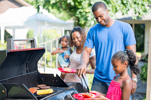 Photo of a family gathered around a barbecue grill, depicting summer food safety tips and guidelines to avoiding foodborne illness, promoting safe and enjoyable outdoor dining during the summer season.